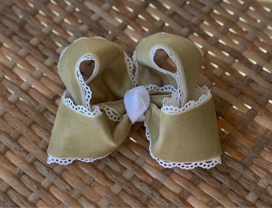 Sage green velvet hair bow with white lace trim and white center wrap, displayed on a woven wicker surface in natural light.