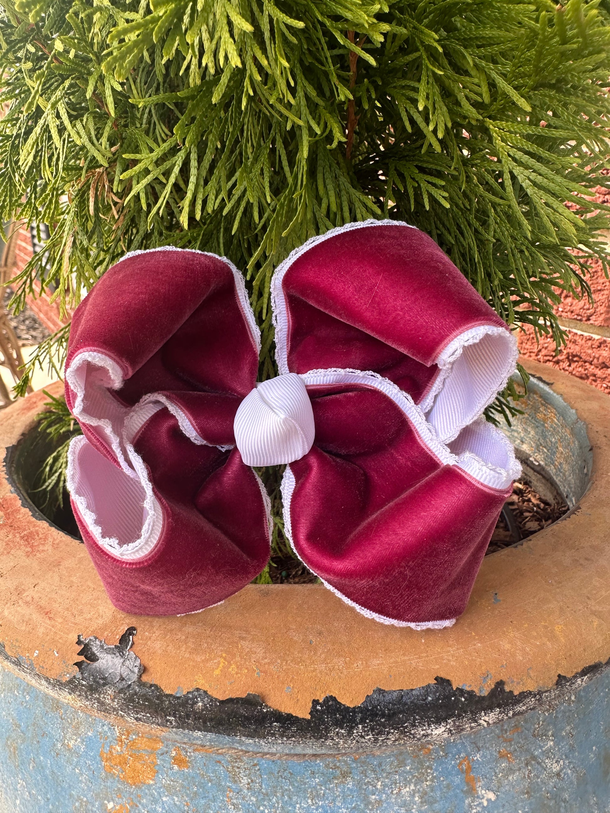 	Crimson velvet lace-trimmed hair bow with white grosgrain center, photographed in natural daylight with trees and grass in the background.