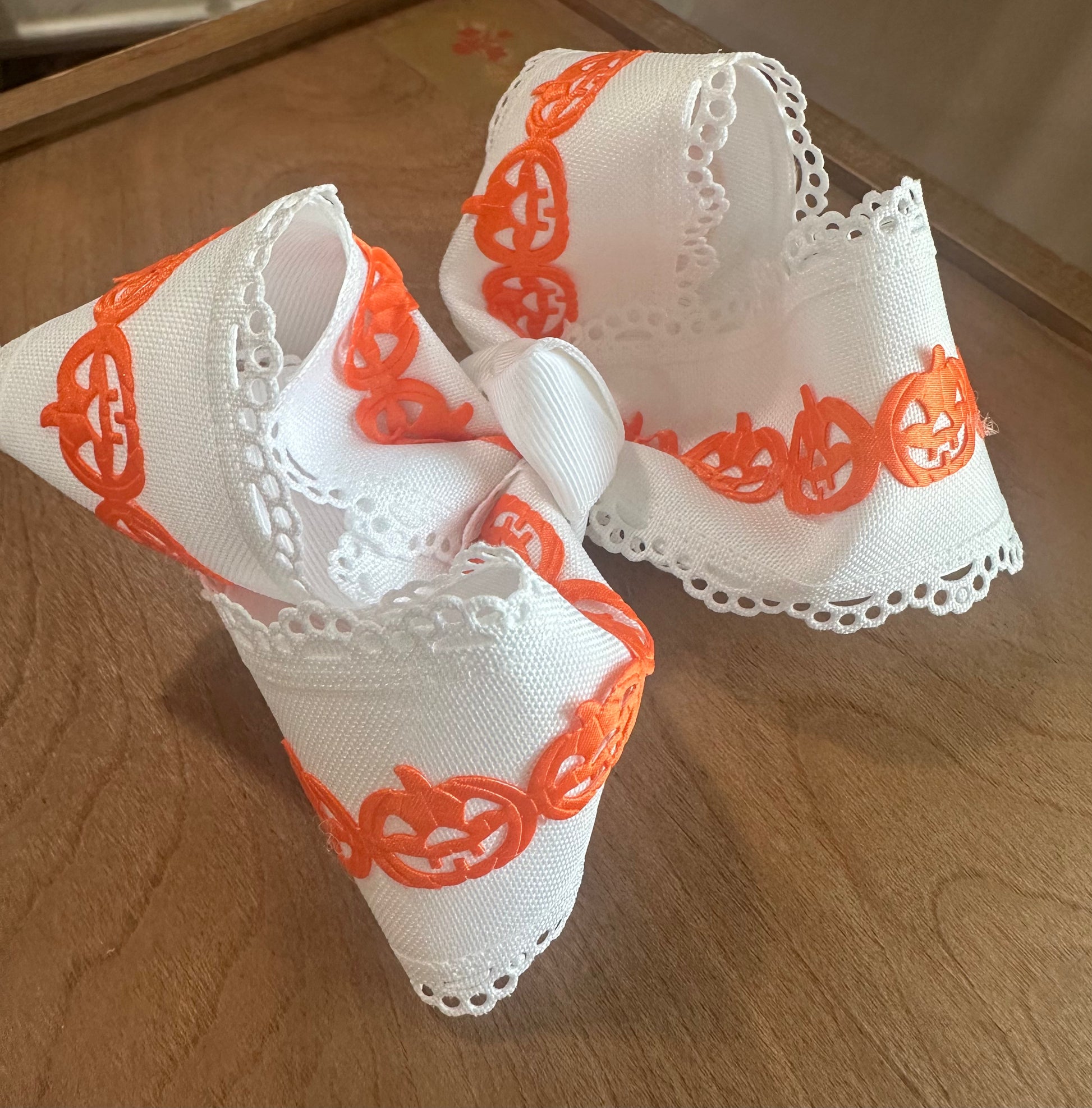 White boutique hair bow with scalloped lace edges and bright orange jack-o-lantern trim design.